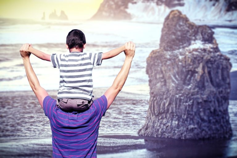padre con figlio sulle spalle in riva al mare - festa del papà